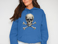 A woman with long brown hair stands against a white background, wearing a Garment Graphics blue streetwear hoodie featuring a skull and crossbones design. She embodies the edgy yet cozy vibe of comfort hoodies.