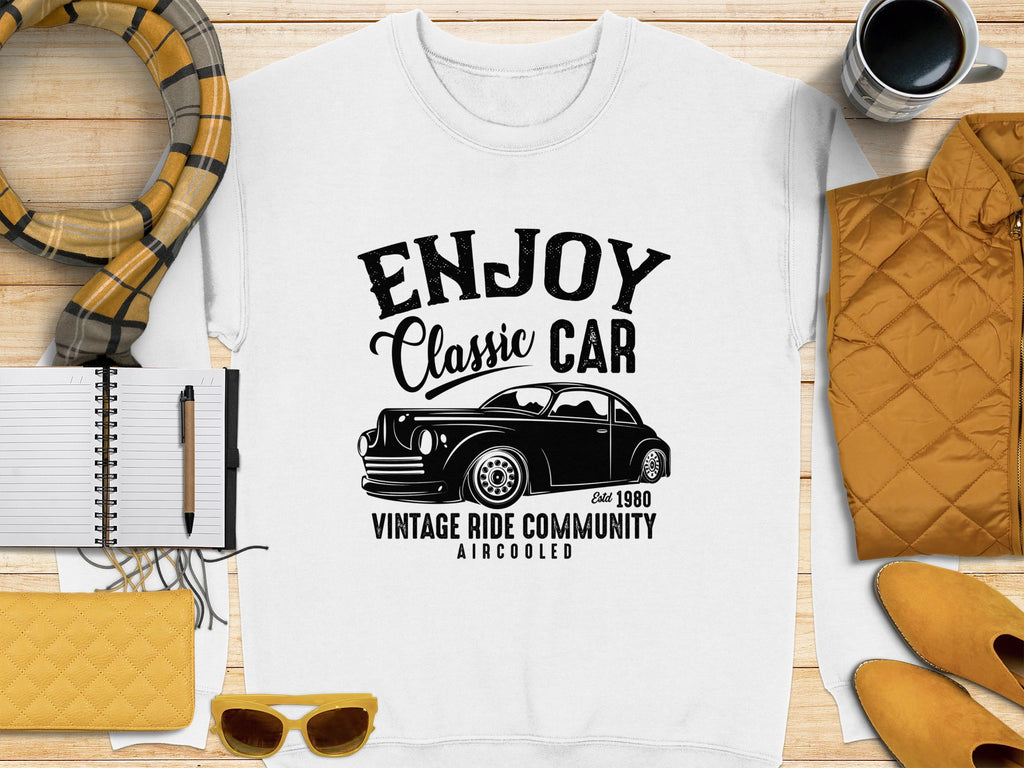 A white t-shirt by Garment Graphics featuring Enjoy Classic Car and a vintage car image is styled with a yellow jacket, scarf, notebook, pen, clutch, sunglasses, coffee mug against a textured backdrop.