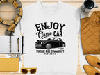 A white t-shirt by Garment Graphics featuring Enjoy Classic Car and a vintage car image is styled with a yellow jacket, scarf, notebook, pen, clutch, sunglasses, coffee mug against a textured backdrop.