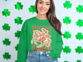 A woman stands before a wall of green shamrocks, embracing the cowboy spirit in a Garment Graphics green sweatshirt featuring a cowboy on horseback and the words Howdy and Not amused. Her long dark hair cascades as she smiles, capturing the joy of rodeo enthusiasts.