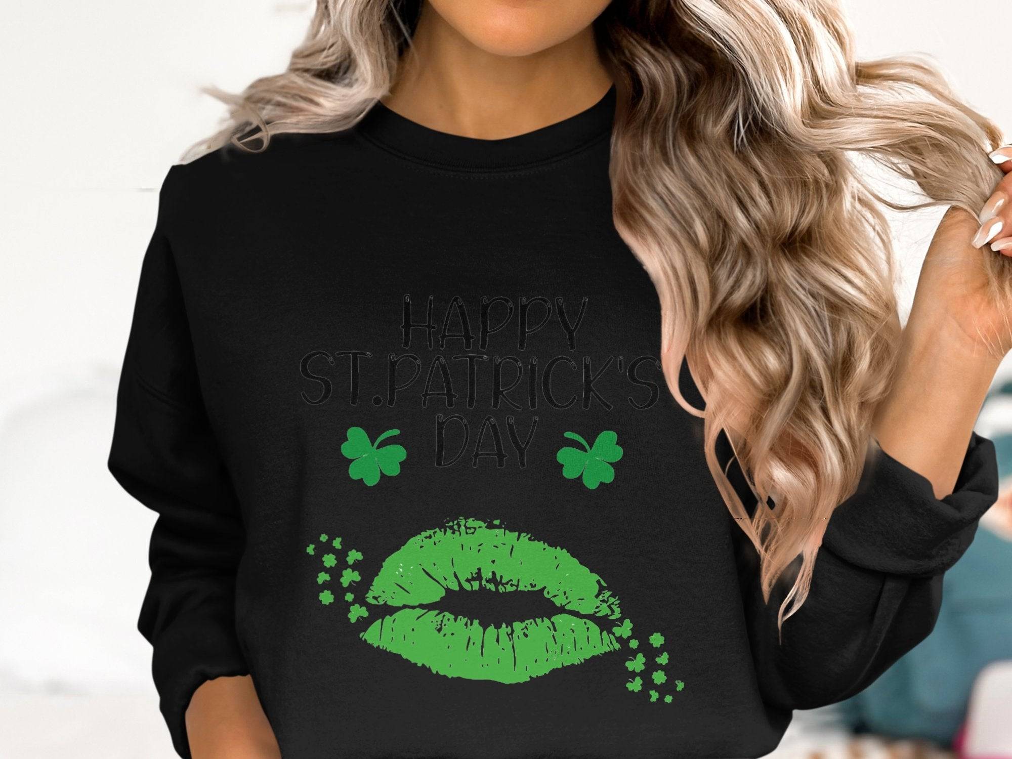 A woman with wavy blonde hair showcases festive cheer in a Garment Graphics black sweatshirt featuring green lips, shamrocks, and Happy St. Patricks Day. Holding a hair strand, she embraces the clover kiss charm of the occasion.