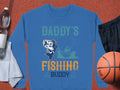 The Garment Graphics blue graphic sweatshirt for outdoor enthusiasts features Daddys Fishing Buddy in vibrant green, blue, and orange with a cartoon fish and person in a boat. Surrounded by items like a basketball, black shorts, white towel, and water bottle, its perfect for any adventure!.