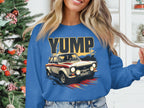 A person is wearing a Garment Graphics blue sweatshirt with a rally car graphic and bold YUMP design, set against the festive backdrop of a decorated Christmas tree and white shelving.