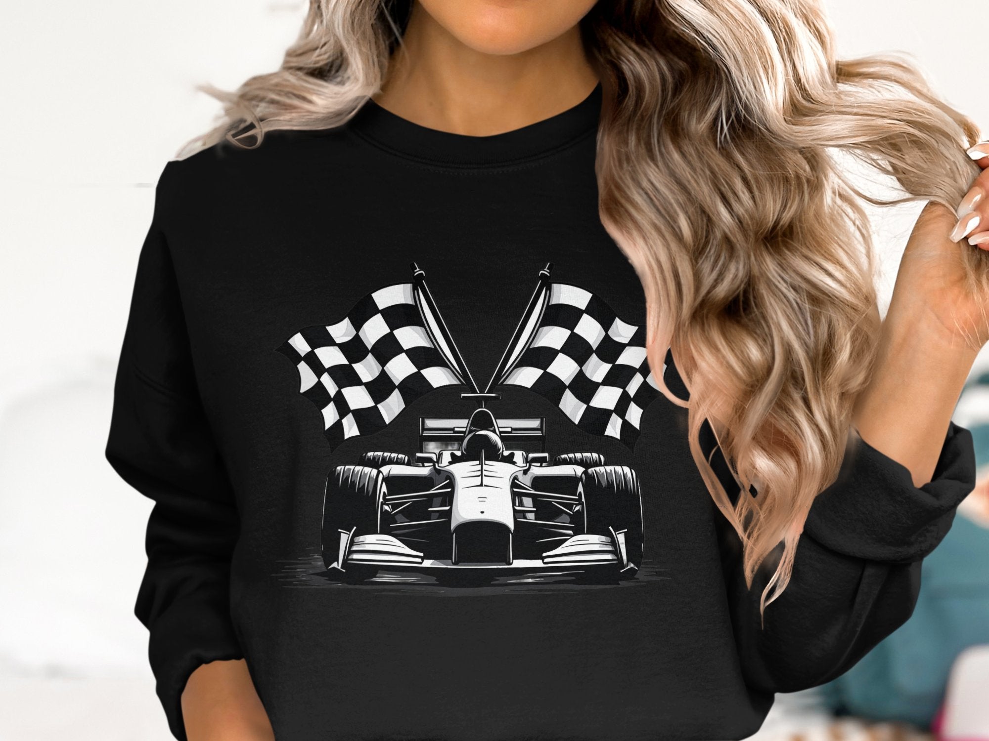 A person with long wavy hair sports a standout design by Garment Graphics—a black sweatshirt featuring a graphic of a Formula 1 car in front of crossed checkered flags, set against a plain light-colored background.