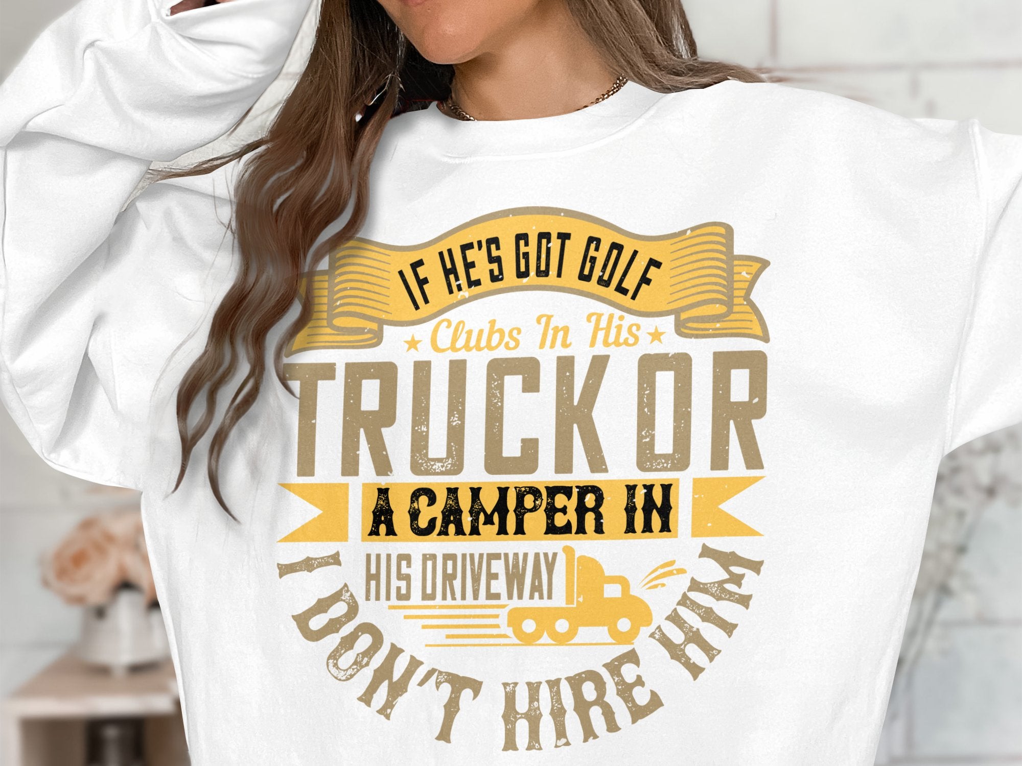 A person, shown from neck to waist, wears a humorous Garment Graphics sweatshirt. The text says: If hes got golf clubs in his truck or a camper in his driveway, I dont hire him in yellow and brown fonts.