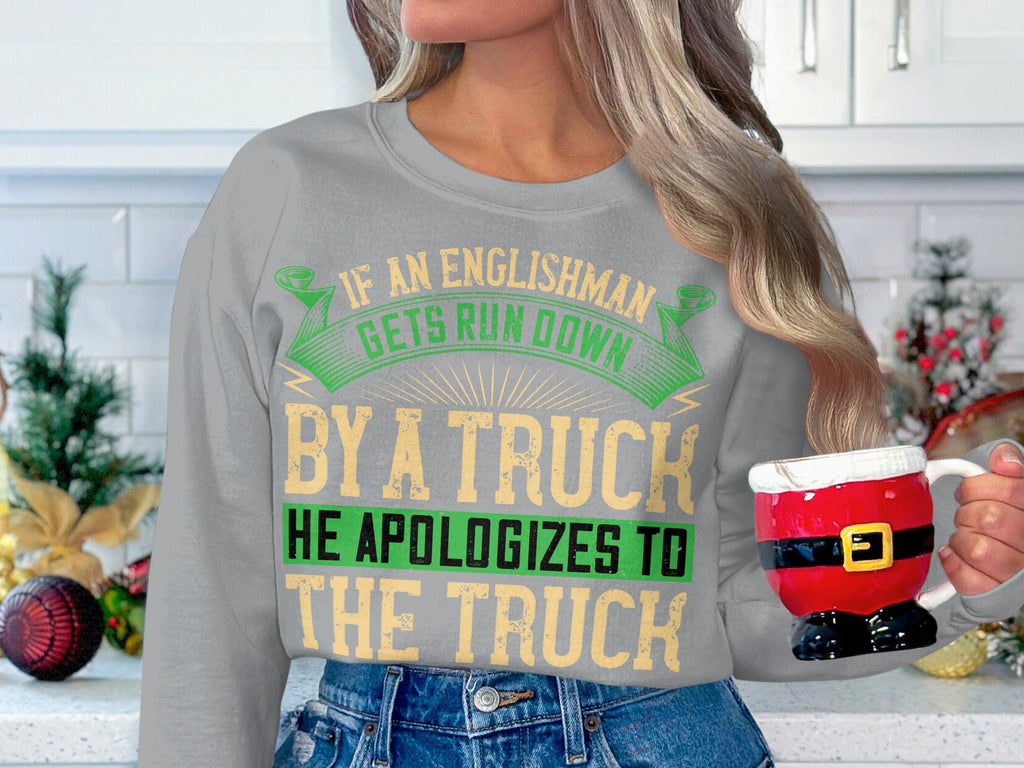 In a festive kitchen, someone holds a Santas pants mug and wears a Garment Graphics sweatshirt with the humorous quote, If an Englishman gets run down by a truck, he apologizes to the truck, available in unisex sizes for everyones enjoyment.