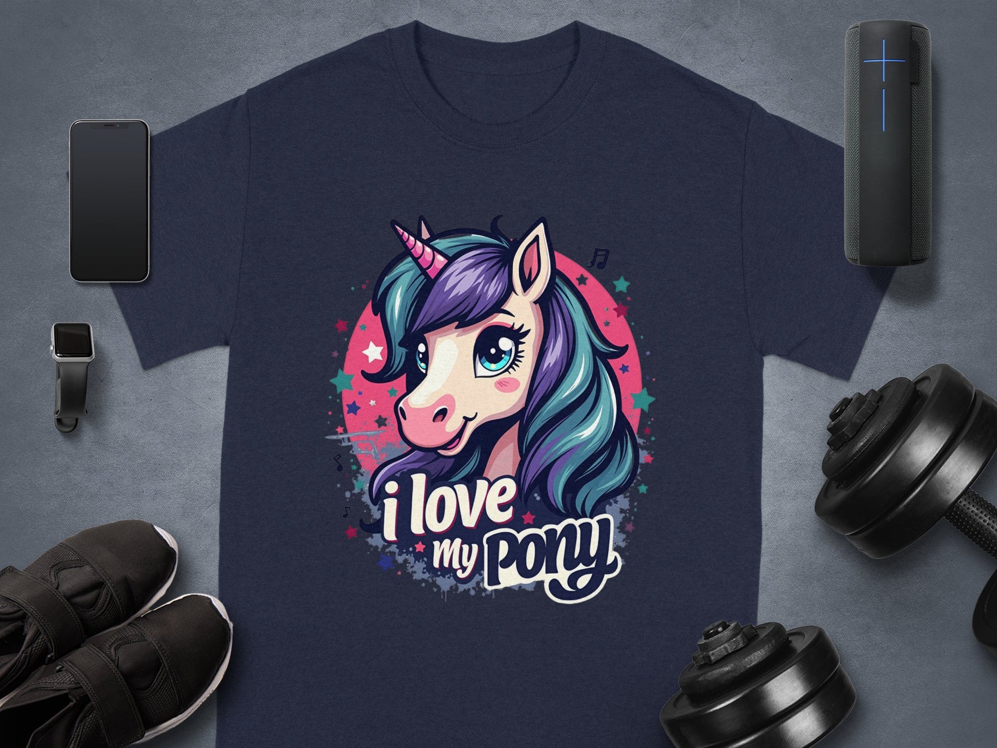 Garment Graphics navy Unicorn T-shirt showcases a vibrant cartoon unicorn and I love my pony text. Perfect for unicorn fans, its paired with essentials like sneakers, a smartphone, smartwatch, portable speaker, and dumbbells on a gray surface.