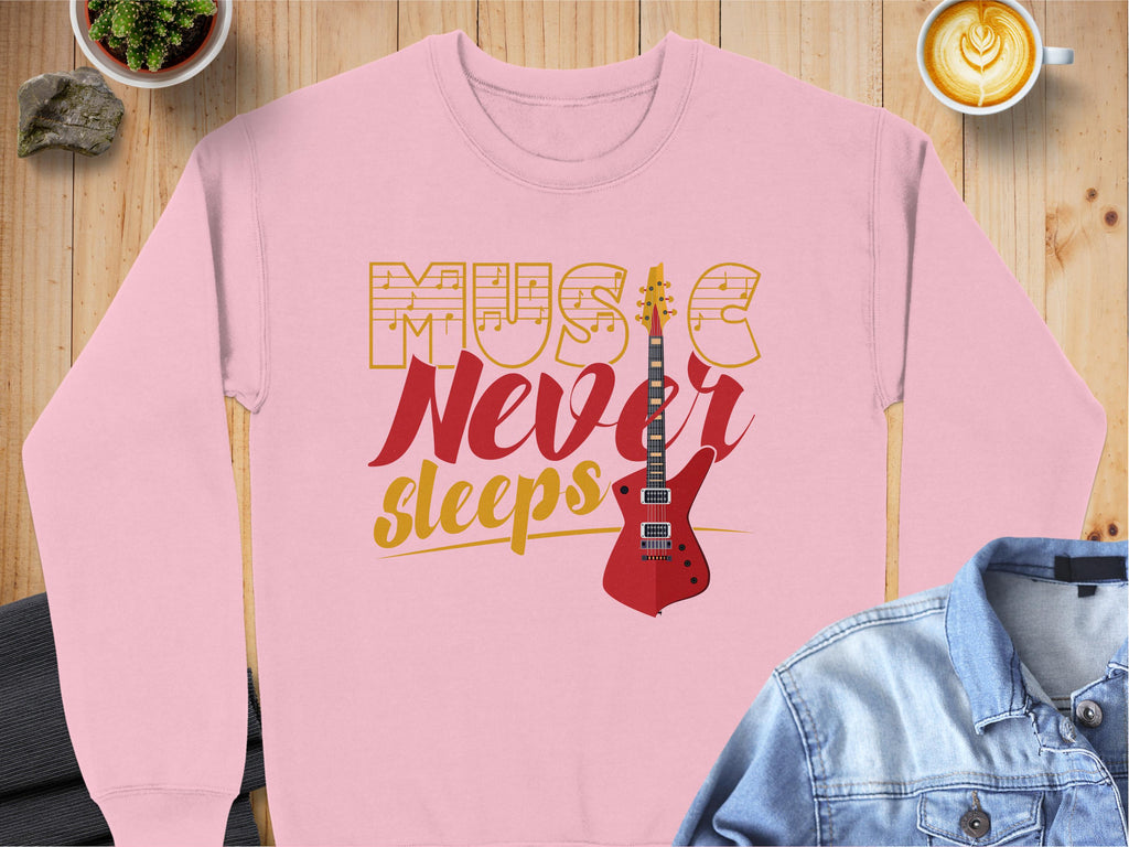 Garment Graphics pink guitar-themed sweatshirt features MUSIC Never sleeps in stylized font with a vivid red electric guitar graphic. Ideal for music lovers, it rests on a wooden surface beside a potted plant, latte, jacket, and small stone.