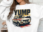 Someone wears a white sweatshirt from Garment Graphics featuring a dynamic YUMP rally car graphic with dust trails, capturing the thrill of speed. Bold black and gold YUMP letters above express the excitement and style unique to these sweatshirts.