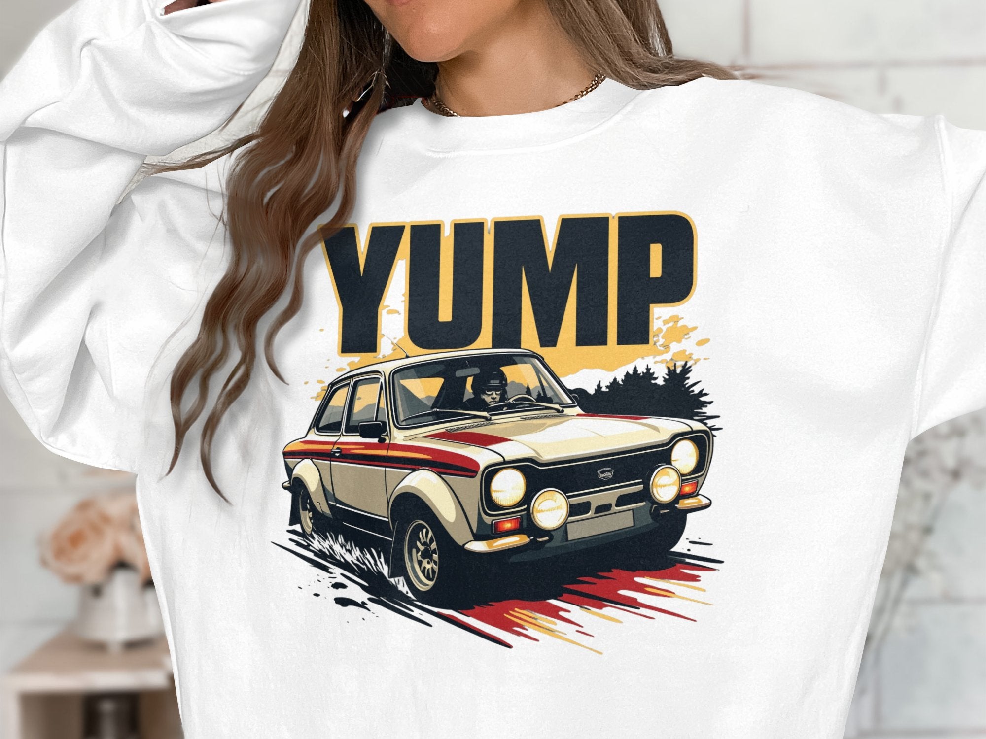 Someone wears a white sweatshirt from Garment Graphics featuring a dynamic YUMP rally car graphic with dust trails, capturing the thrill of speed. Bold black and gold YUMP letters above express the excitement and style unique to these sweatshirts.