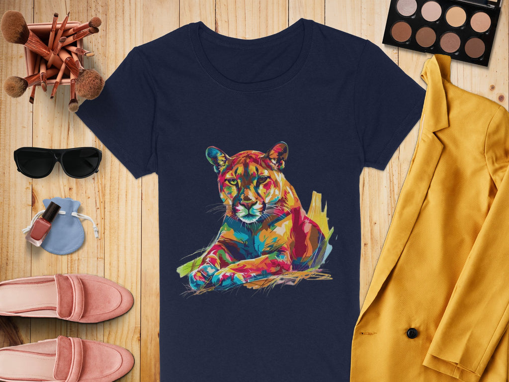 A flat lay image featuring Garment Graphics navy T-shirt with a colorful puma design, complemented by a yellow jacket, makeup palette with brushes, sunglasses, pink shoes, nail polish, and a small blue purse on a wooden background.