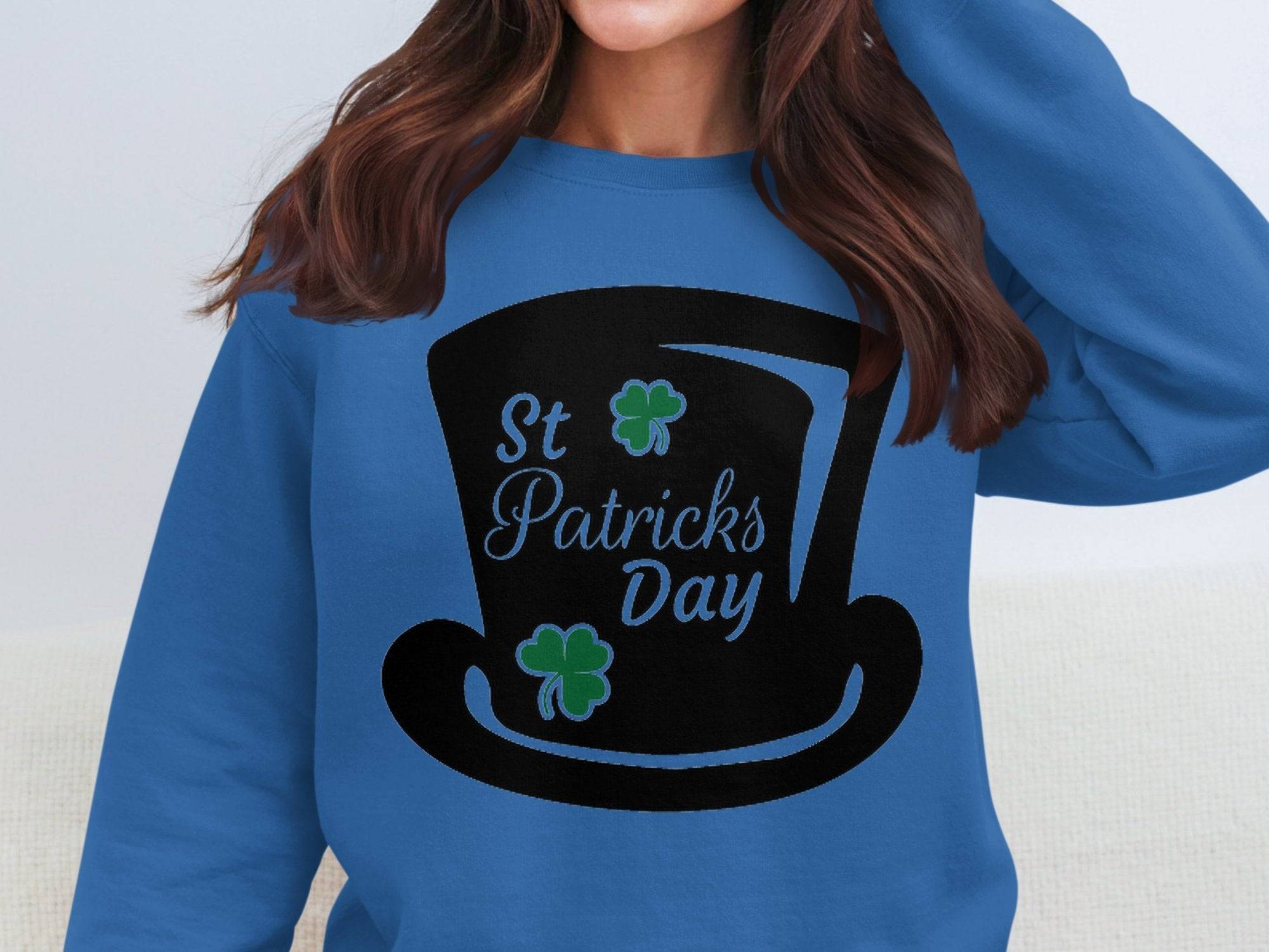 A person with long brown hair is wearing a stylish blue sweatshirt by Garment Graphics. It features a black graphic of a top hat adorned with two green shamrocks and the text St. Patricks Day, capturing the festive spirit perfectly.