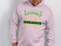 A person wearing a Garment Graphics light pink hoodie sports a green and yellow quote: If an Englishman gets run down by a truck he apologizes to the truck. The humorous text highlights English etiquette as the wearer looks downward.