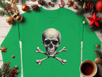 A Garment Graphics green shirt featuring a skull and crossbones design is showcased on a wooden surface, surrounded by festive Christmas elements like pine branches, ornaments, a candy cane, and a steaming cup of tea for a mix of holiday cheer and daring style.