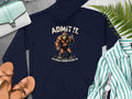 A Garment Graphics navy hoodie with a Bigfoot illustration and ADMIT IT. LIFE WOULD BE BORING WITHOUT ME. text rests on gray, surrounded by a green and white striped shirt, tan sandals, a watch, and classic handbags for an effortlessly stylish look.