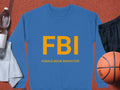Garment Graphics offers a blue unisex sweatshirt featuring bold yellow FBI (Female Boob Inspector) letters. Set on a red surface, it complements a basketball, black shorts, towel, and water bottle.