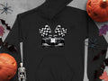 A Garment Graphics black hoodie, featuring a race car and checkered flags, is artistically placed among pumpkins, bats, a skeleton, and autumn leaves on a gray surface for an exciting racing theme with a spooky Halloween twist.