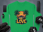 A green sweatshirt by Garment Graphics, featuring palm trees, a sunset, and One Love at the center, is displayed alongside a smartphone, smartwatch, speaker, dumbbells, and black sneakers.
