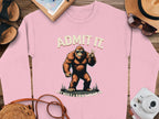 This pink Garment Graphics sweatshirt showcases a playful Bigfoot flashing a peace sign with the words Admit It above and Life Would Be Boring Without Me below. Unisex sizing makes it ideal for casual wear, paired with essentials like a camera, hat, sunglasses, notebook, and sandals.
