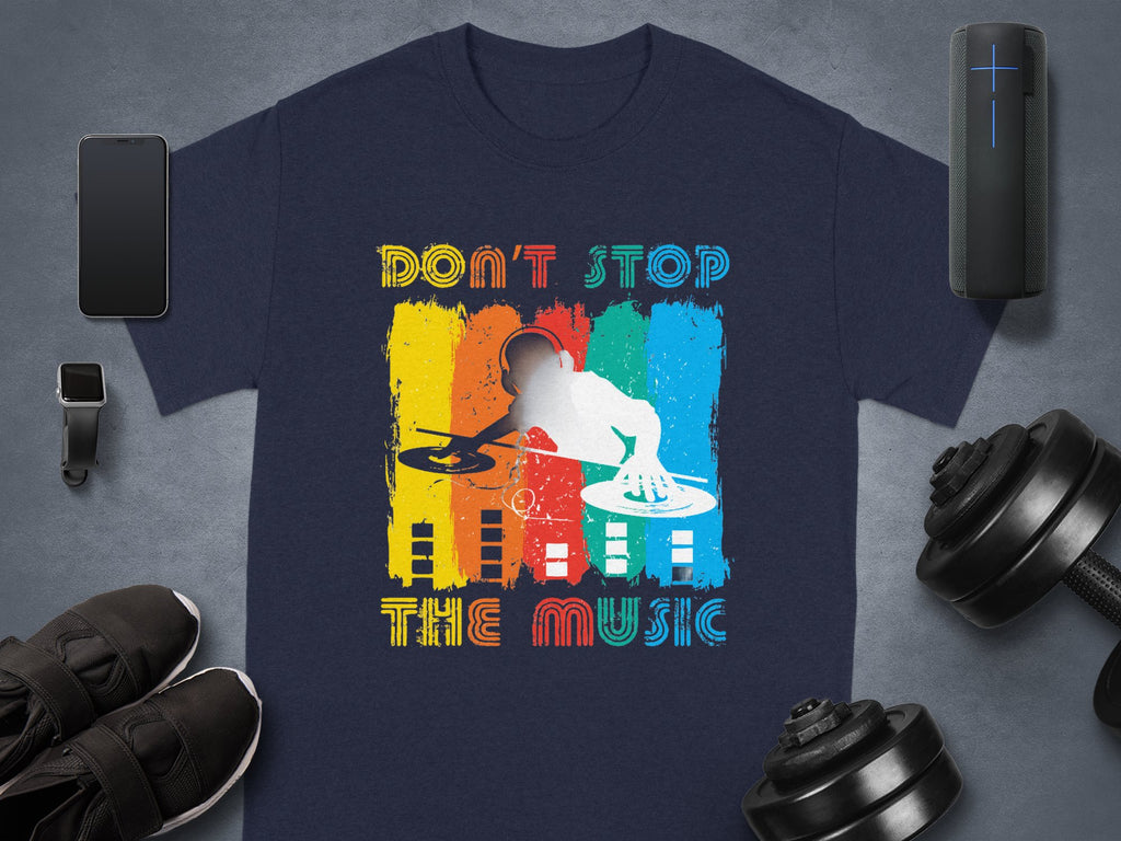 A Garment Graphics T-shirt featuring a DJ graphic and Dont Stop the Music slogan, ideal for music fans, lies on a gray background with a smartphone, smartwatch, shoes, portable speaker, and dumbbells. The design is vibrant with colorful elements.