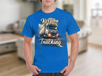 A person wearing a blue Garment Graphics T-shirt featuring a large truck and the phrase Keep on Trucking, ideal for truck enthusiasts, stands in a blurred indoor setting.