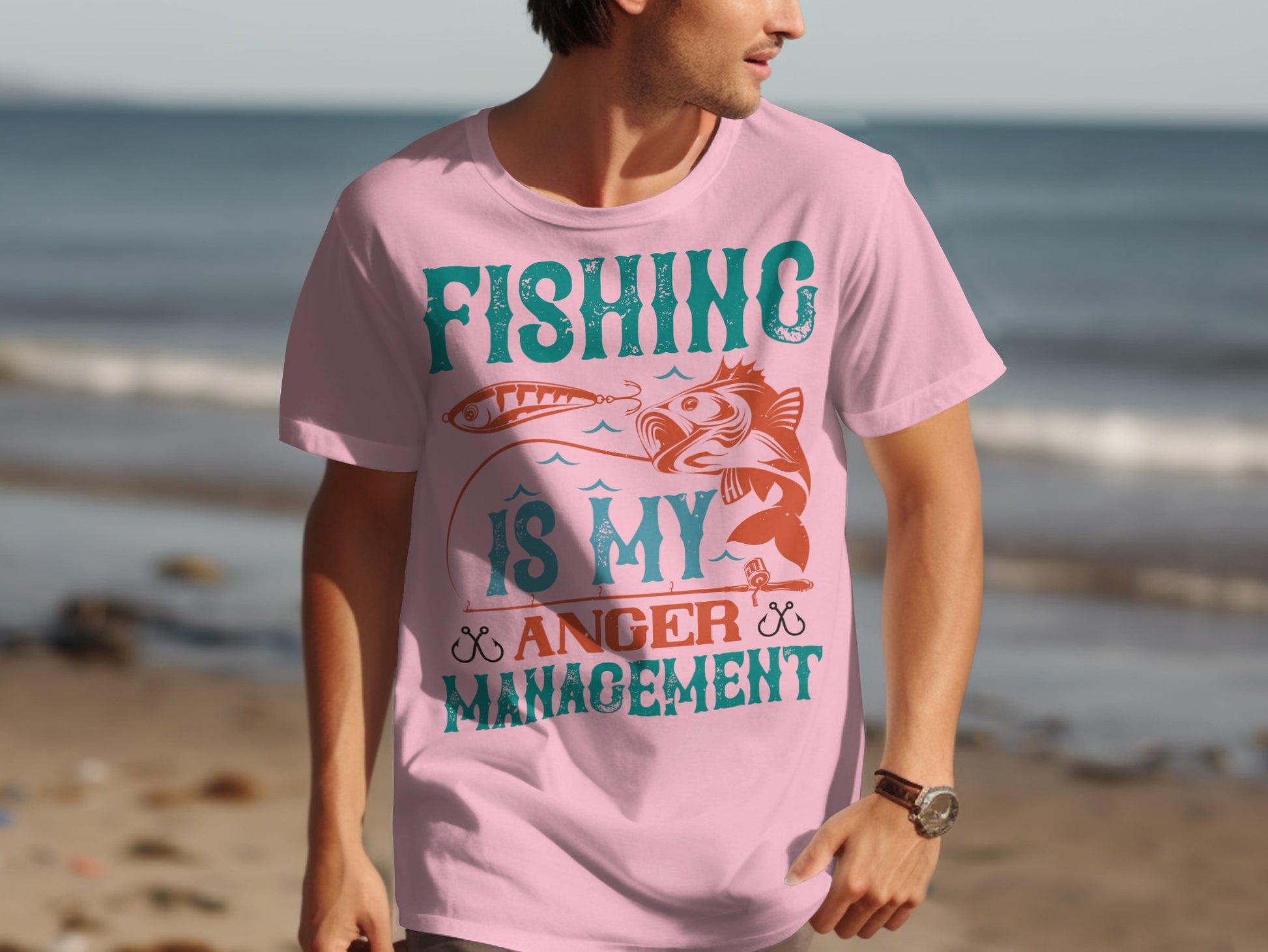 A fishing enthusiast at the beach wears a Garment Graphics pink T-shirt with Fishing is My Anger Management, alongside a fish and fishing lure design.