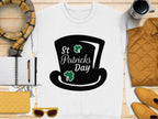 A flat lay image showcases Garment Graphics stylish sweatshirt featuring a black top hat graphic with St Patricks Day and green shamrocks, paired with yellow sunglasses, a scarf, a pen on a notebook, a yellow bag, a jacket, and a coffee cup to capture the festive spirit.