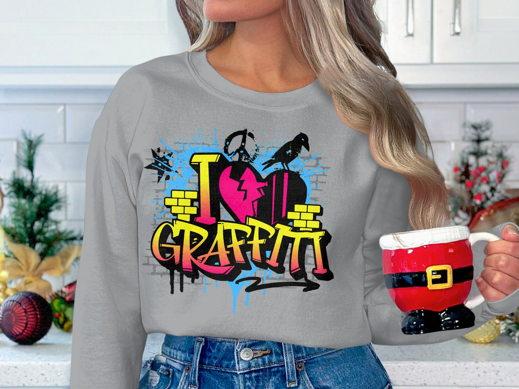 In a festive kitchen, someone holds a Santa-themed mug while wearing Garment Graphics grey sweatshirt, featuring the vibrant I Love Graffiti design with a colorful heart and paint splatters that showcase urban style.