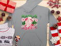 A gray hoodie from Garment Graphics, featuring a festive design with Hands Off! in green and red, showcases a person in a cowboy hat surrounded by flowers and hearts. Its styled for the wild Graphic Hoodies look and is laid on a wooden surface with holiday decorations.