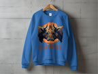 A loose-fit blue sweatshirt featuring a bullocks graphic of a bulls head in an orange circle hangs on a wooden hanger against a concrete wall. The bold BULLOCKS text enhances its allure. Brand: Garment Graphics.