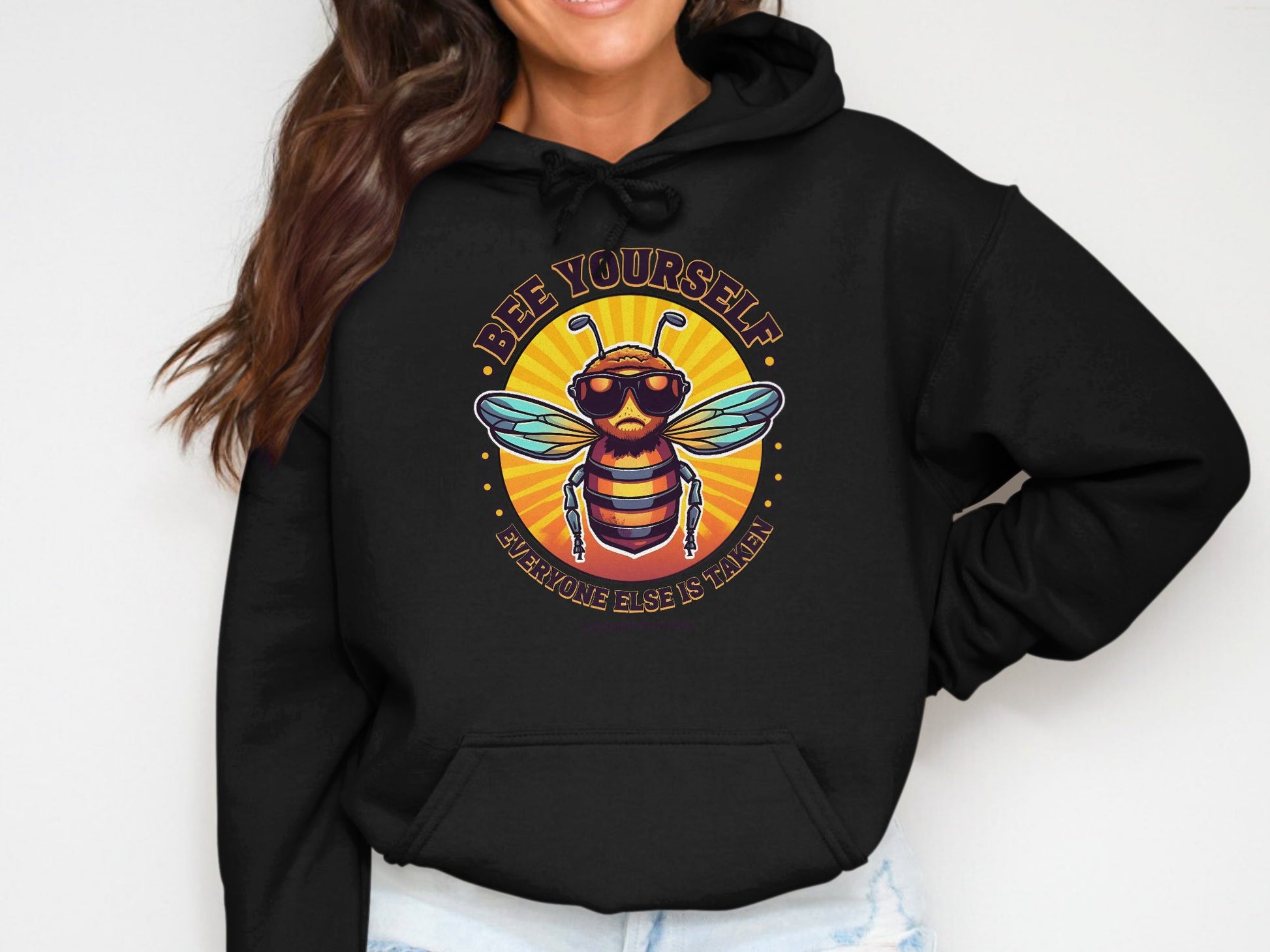 Dressed in a Garment Graphics black Bee Yourself hoodie displaying a bee with sunglasses and the phrase Bee Yourself, Everyone Else is Taken, the person keeps their face hidden with long, wavy hair, creating an eye-catching style.