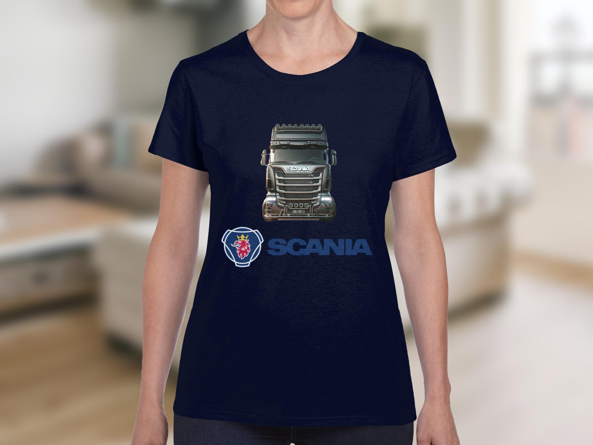 A person is wearing a dark blue Garment Graphics T-shirt featuring a striking truck graphic and logo. The detailed truck image adorns the chest, ideal for automotive fans. The background is a softly blurred indoor setting.