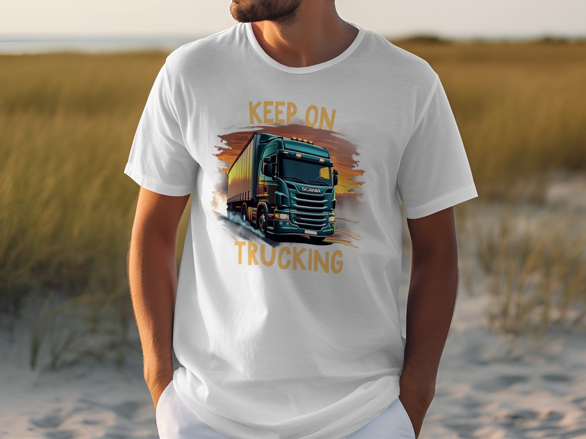 Someone wearing a white Garment Graphics shirt featuring a big green truck and the phrase KEEP ON TRUCKING stands outside among sandy ground and tall grasses, an ideal backdrop for truck lovers.