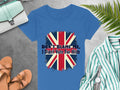 Garment Graphics blue T-shirt, made of 100% cotton, features the Union Jack and DONT BLAME ME, I Didnt Vote For Him text. Its artfully displayed on a grey surface with a green-striped shirt, tan sandals, a wristwatch, purse, and fern leaves.