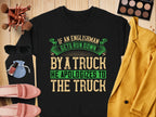 The Garment Graphics black sweatshirt showcases a bold, humorous green and beige text: If an Englishman gets run down by a truck, he apologizes to the truck. Styled unisex on wood with accessories like makeup, sunglasses, and clothes.