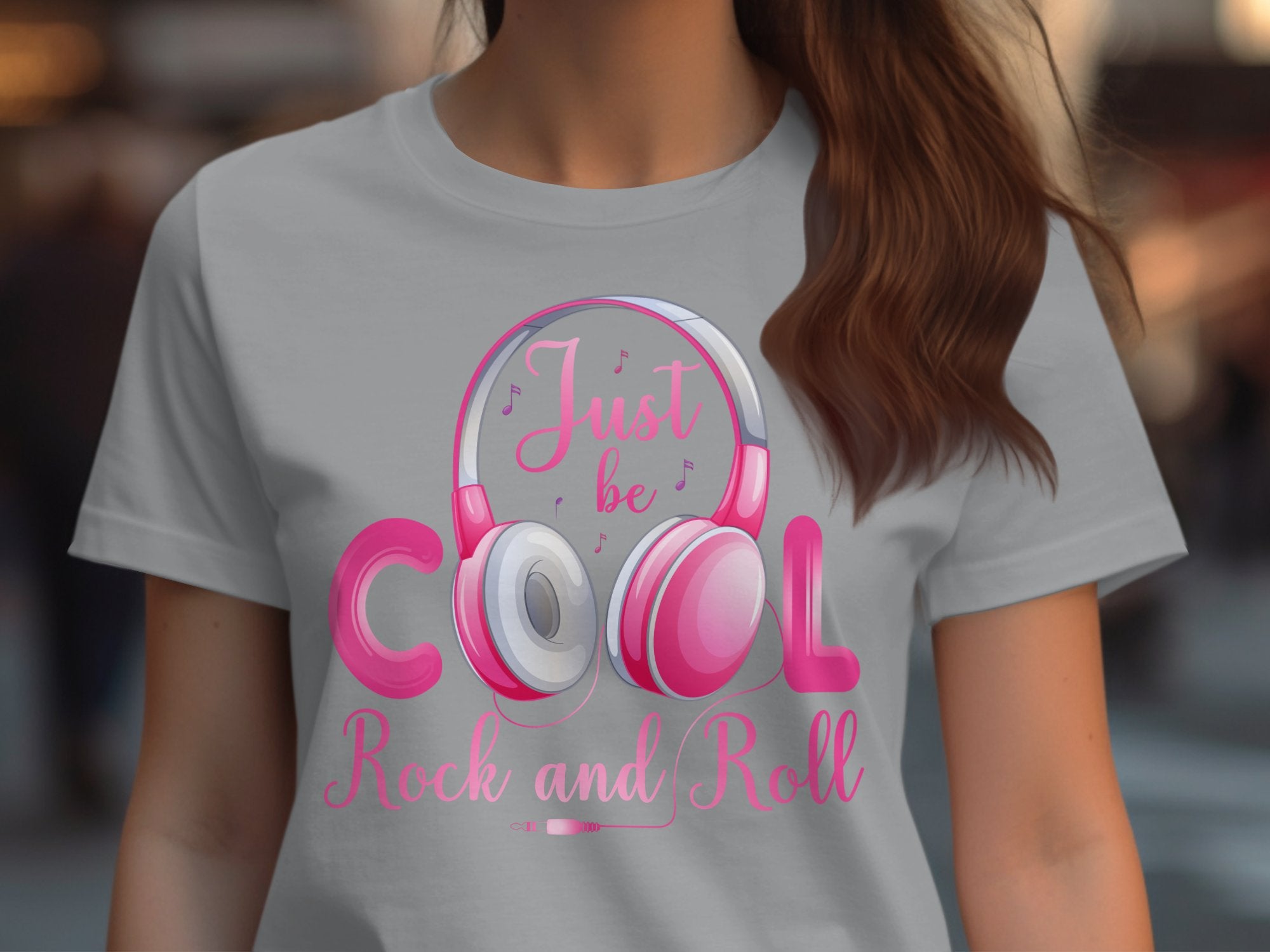 Someone sports a Garment Graphics gray tee featuring pink and white headphones, with vibrant pink and red text reading Just be Cool Rock and Roll, ideal for music lovers embracing rock and roll vibes.