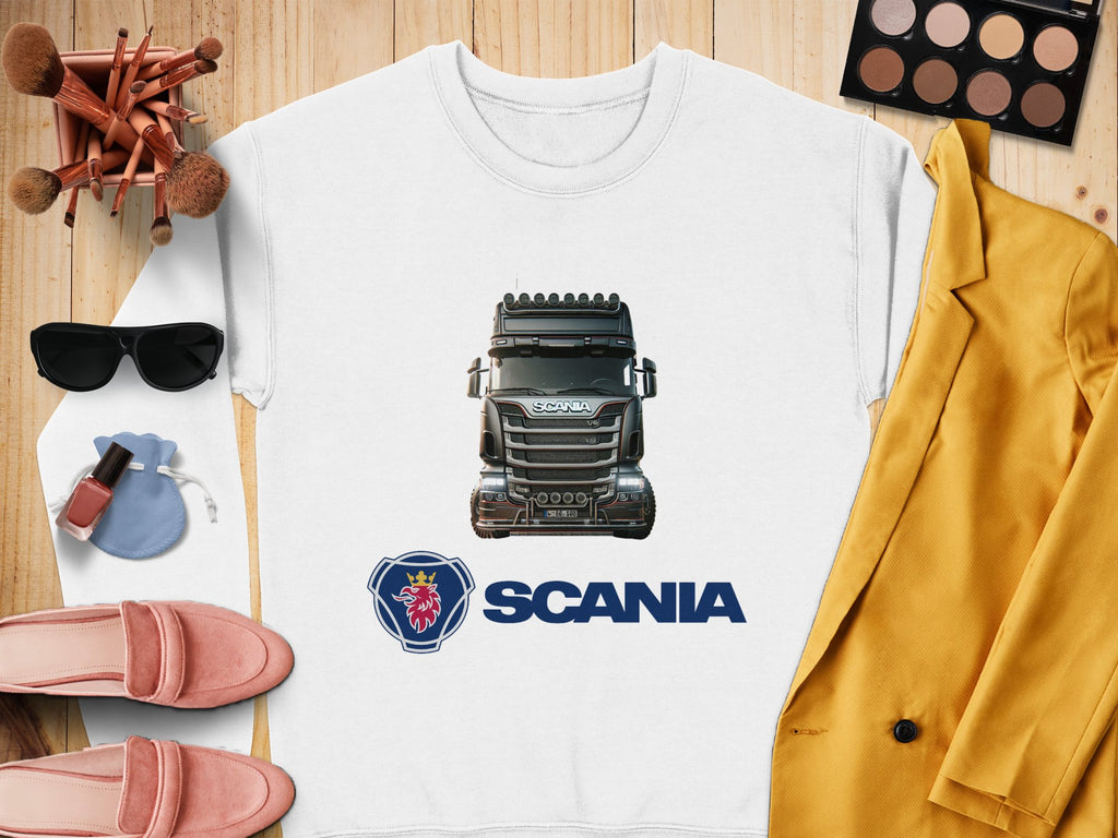 The graphic crewneck sweatshirt by Garment Graphics, featuring a Scania truck image and logo, is displayed on a wooden surface with pink shoes, sunglasses, makeup brushes, a makeup palette, nail polish, a pink velvet pouch, and a mustard-yellow jacket—ideal for stylish truck enthusiasts.