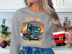 A person sports a Garment Graphics grey sweatshirt featuring Keep On Trucking and a truck image, ideal for truck fans. Theyre holding a Santa outfit-themed mug in a white kitchen decked out with Christmas decor.