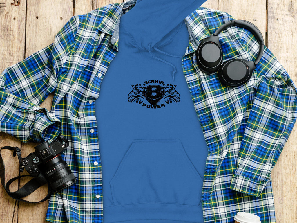 A blue Garment Graphics hoodie featuring a bold Scanir Power logo lies next to a coordinating blue and green plaid shirt, headphones, a camera, and a white cup on wood. This classic fit ensemble exudes style and comfort.