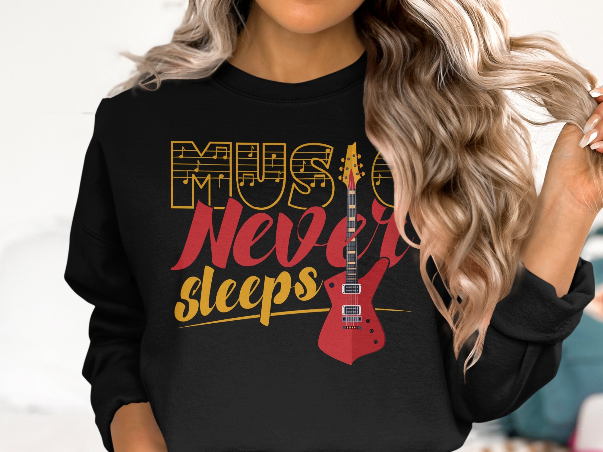 A person with wavy hair wears a Garment Graphics sweatshirt, featuring Music Never Sleeps in decorative fonts and a bold red electric guitar illustration, perfect for music lovers. They casually twirl a strand of their hair.