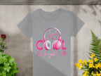 Garment Graphics offers a gray t-shirt with a vibrant Just be Cool Rock and Roll design, featuring pink and white headphones. This shirt is perfect for music lovers, displayed on concrete, surrounded by lush green plants and bright yellow flowers.