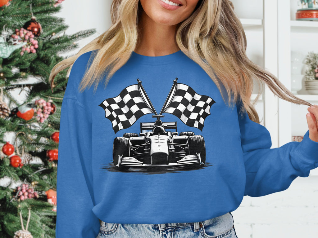 A person in a Garment Graphics standout racing car sweatshirt featuring a checkered flag print stands by a decorated Christmas tree with white shelves displaying small potted plants and a book in the background.