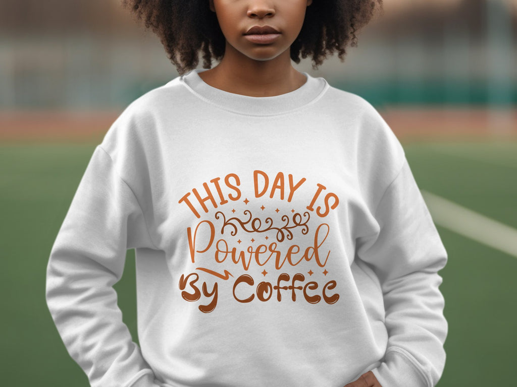 A person is seen wearing a Garment Graphics sweatshirt featuring This Day is Powered by Coffee in brown and orange with swirls and stars, standing out against a blurred outdoor backdrop.