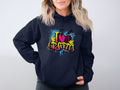 A person wears a navy hoodie from Garment Graphics, featuring a vibrant I Heart Graffiti design in yellow, pink, and blue. It seamlessly integrates urban street art into casual wear with splashes and brick patterns in the background.