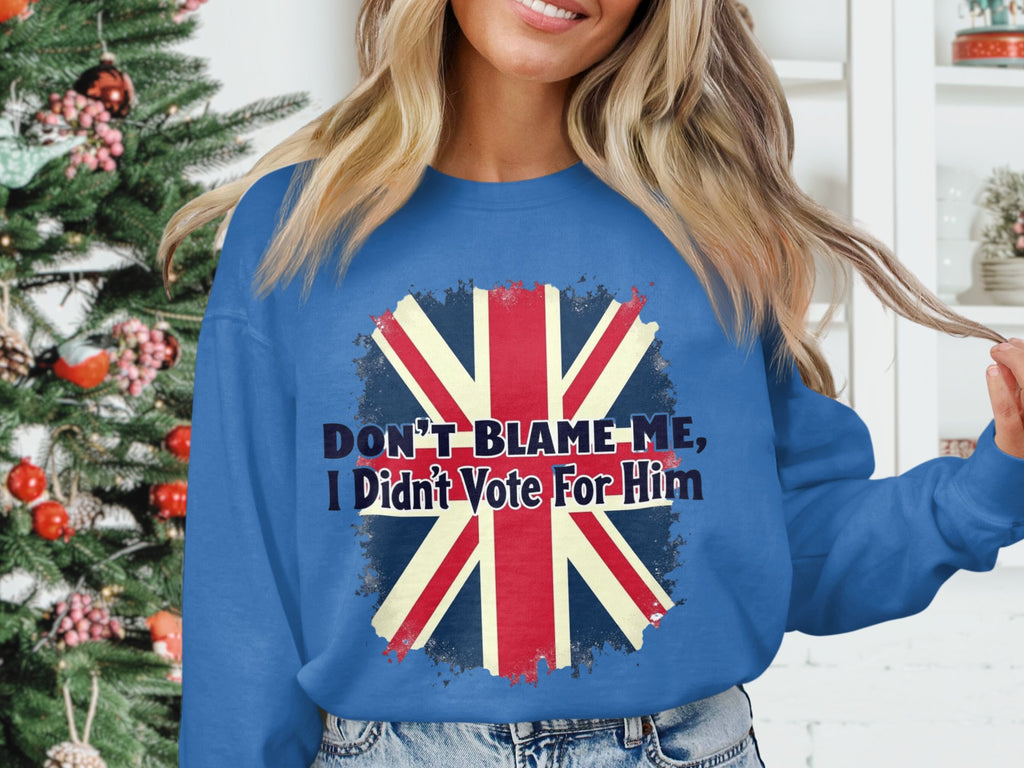 A person in a Garment Graphics blue sweatshirt with the Union Jack and Dont Blame Me, I Didnt Vote For Him stands by a Christmas tree with red and white decorations. This unisex sweatshirt ensures a comfortable fit.
