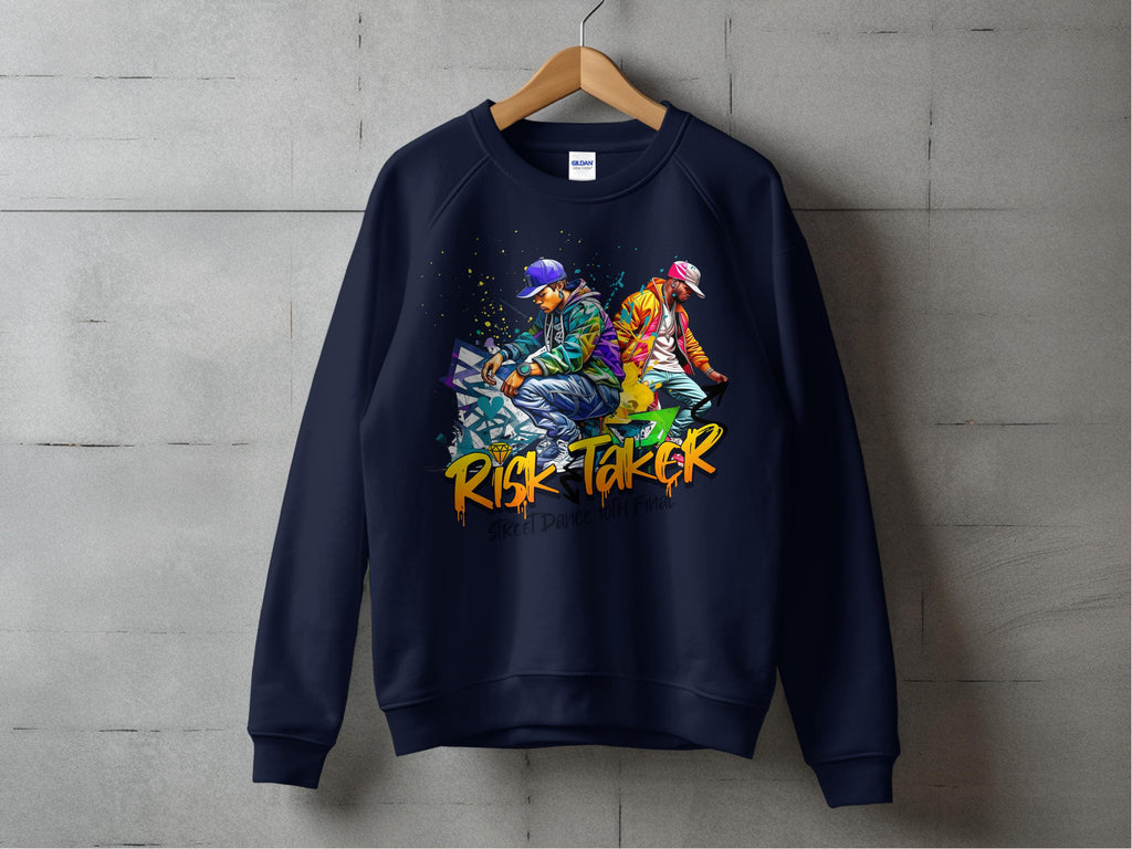 A navy sweatshirt by Garment Graphics hangs on a wooden hanger against a concrete wall, with street dance graphics of two people back-to-back. Risk Taker is boldly printed in orange below the image. The unisex design embodies urban style.