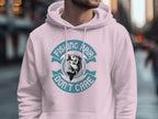 In an urban setting, someone sports a Garment Graphics light pink hoodie with the phrase Fishing Hair Dont Care and an anglers catch at its center. The blurred background highlights city buildings.