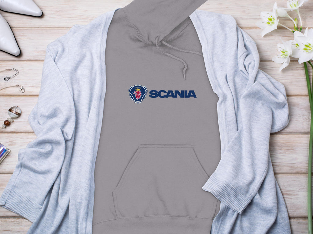 A trendy Garment Graphics hoodie peeks from beneath a light blue cardigan, all beautifully displayed on a wooden surface. White flowers, elegant jewelry, and stylish high-heeled shoes surround this chic ensemble for a perfect blend of casual and sophisticated fashion.