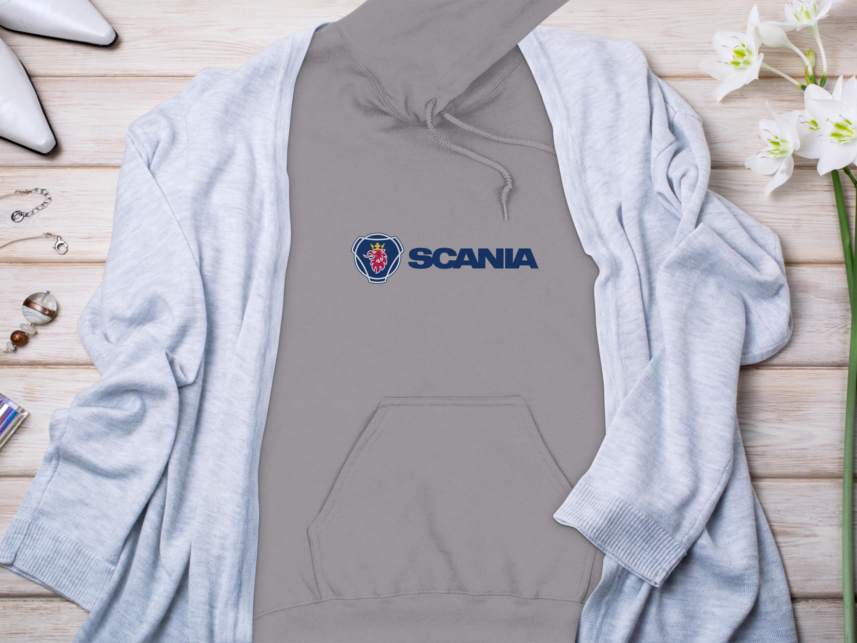 A trendy Garment Graphics hoodie peeks from beneath a light blue cardigan, all beautifully displayed on a wooden surface. White flowers, elegant jewelry, and stylish high-heeled shoes surround this chic ensemble for a perfect blend of casual and sophisticated fashion.