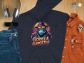 A vibrant black hoodie from Garment Graphics displays a gorilla wearing sunglasses and a hat with Gorilla Gangster text, paired with streetwear staples like headphones, keys, sunglasses, jeans, an orange shirt, and a watch on wood.